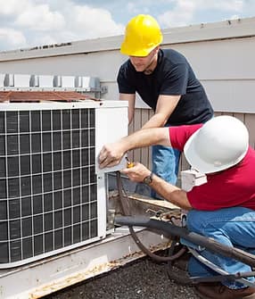 Two workers servicing an HVAC unit — trade work by Treacy Brothers crew